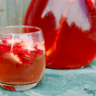 strawberry wine sangria in a clear rounded glass with sliced of fresh strawberries on a green marbled tile