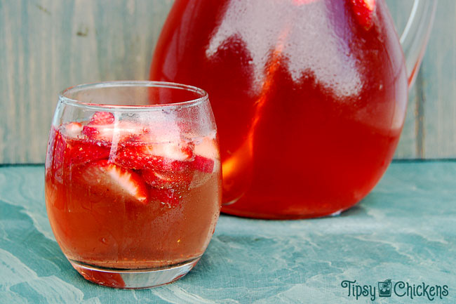 strawberry wine sangria in a clear rounded glass with sliced of fresh strawberries on a green marbled tile