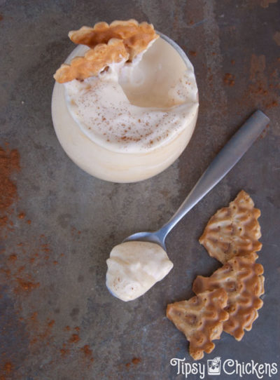 top view of glass of rumchata mousse with a spoonful scooped out on a spoon sitting on a mottled tile with sprinkles cinnamon and broken up pieces of vanilla pizzelle