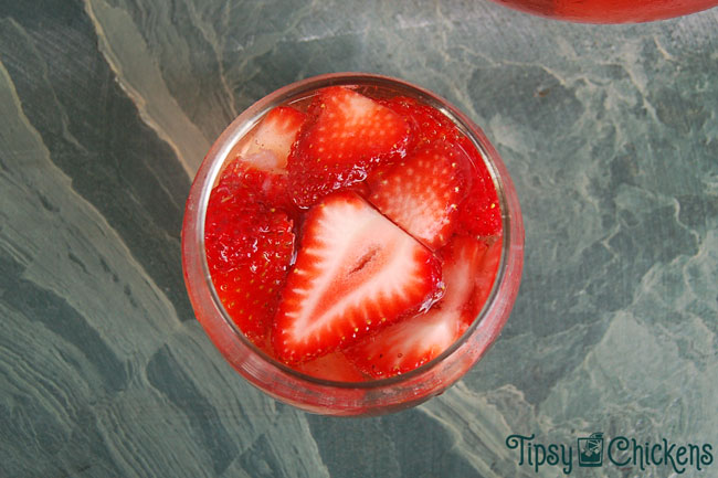 strawberry wine sangria in a clear rounded glass with sliced of fresh strawberries on a green marbled tile