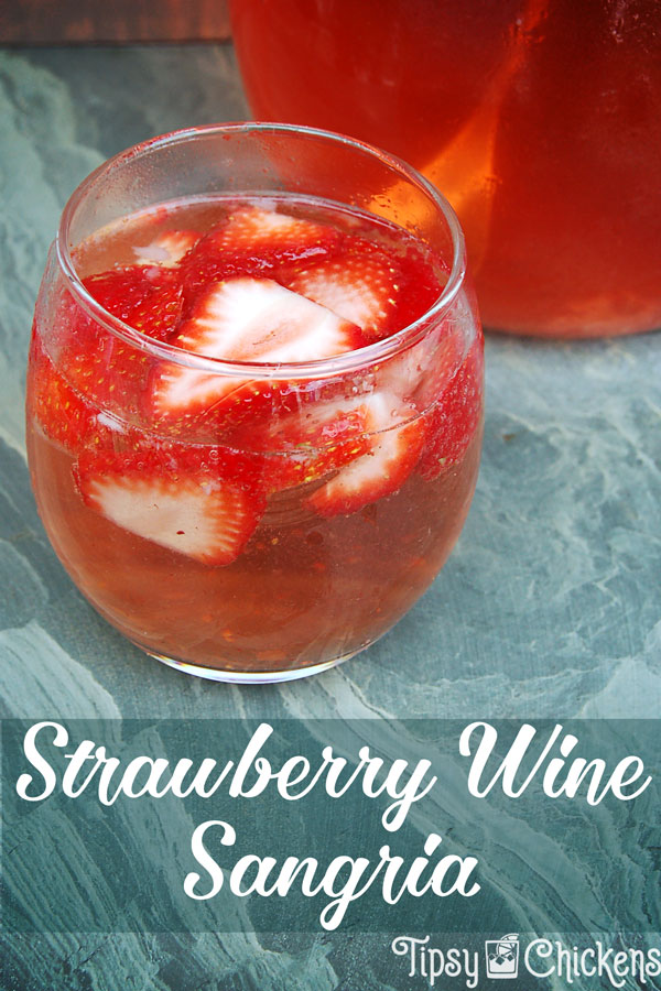 strawberry wine sangria in a clear rounded glass with sliced of fresh strawberries on a green marbled tile