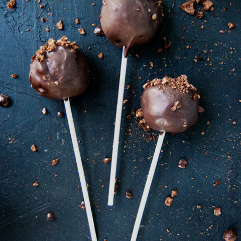 three chocolate covered cake pops laying on a black background surrounded by fragments of crushed chocolate covered espresso beans