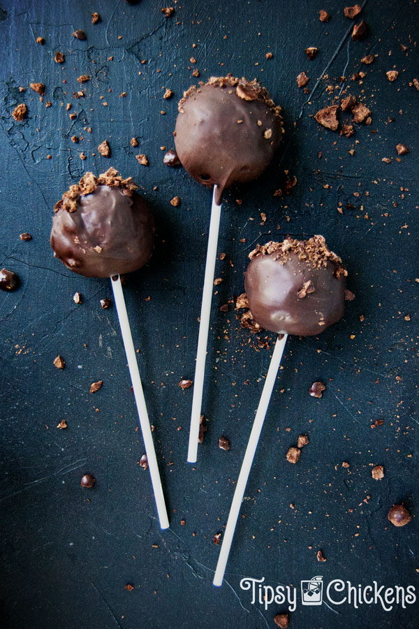 three chocolate covered cake pops laying on a black background surrounded by fragments of crushed chocolate covered espresso beans