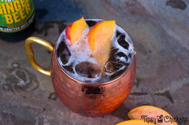 each Moscow mule in hammered copper cup with peach slice garnish and saranac ginger beer in the background