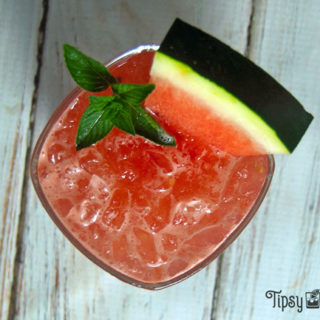 watermelon gin smash in a square rocks glass with a slice or watermelon and a sprig of mint