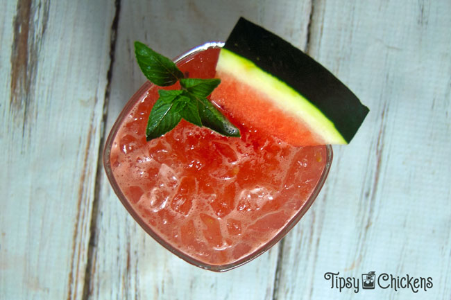 watermelon gin smash in a square rocks glass with a slice or watermelon and a sprig of mint