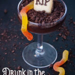 coupe glass filled with spiked arck chocolate pudding with crushed oreos, gummy worms and a Milano cookie turned into ta tombstone with RIP written in chocolate