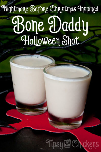 two shot glasses filled with white Bone Daddy Shots made from rumchata and black rum sitting on a red blood splatter coaster with a bright green bachground with spooky black branches and text overlay Nightmare Before Christmas Inspired Bone Daddy Halloween Shot