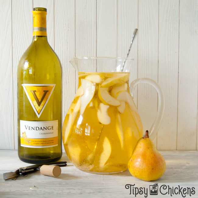 glass pitcher filled with sliced pears and white wine pear sangria with a bottle of chardonnay, a pear and a wine bottle opener