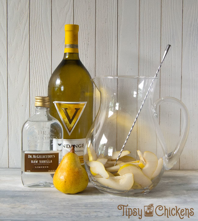 glass pitcher with a bottle of chardonnay, a pear and a bottle of vanilla schnapps