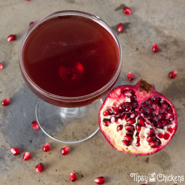 top view of a winter rose cocktail, a jack rose variation with pomegranate juice, shown with half a pomegranate and scattered pomegranate arils