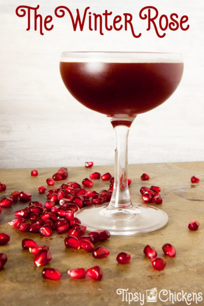 coupe glass filled with winter rose cocktail made with Lairds Applejack Pomegranate juice and grenadine on a stone surface with pomegranate arils