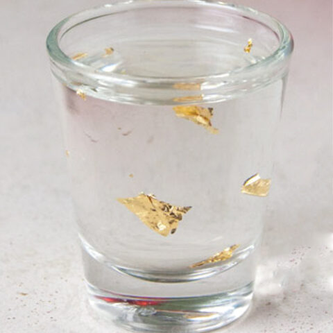single shot glass filled with Goldschläger, Buttershots and edible gold leaf on a white tile surface