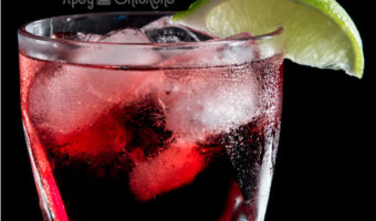 Cranberry and lime cocktail on the rocks in a rocks glass against a black background
