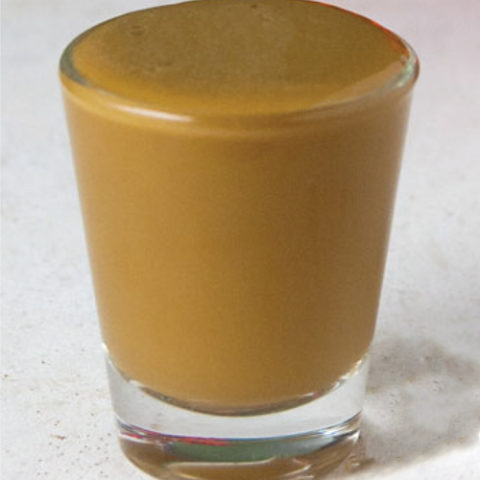 single shot glass filled with eggnog, coffee liqueur and vodka on a white tile surface