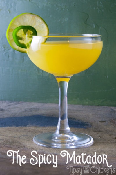 cocktail made with jalapeno tequila, pineapple juice and lime juice with a line wheel and jalapeno garnish against a green background