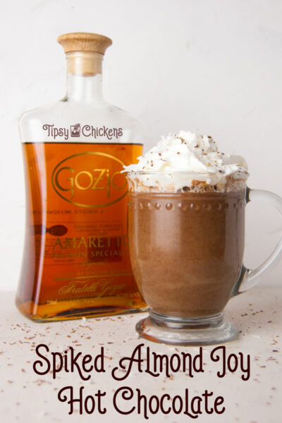 hot chocolate in a glass mug made with coconut milk, bakers chocolate, amaretto and coconut syrup topped with whipped cream and chocolate shavings with amaretto bottle in the background