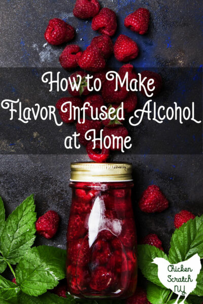 class jar filled with raspberries and vodka against a dark splattered background with raspberries and raspberry leaves in the background