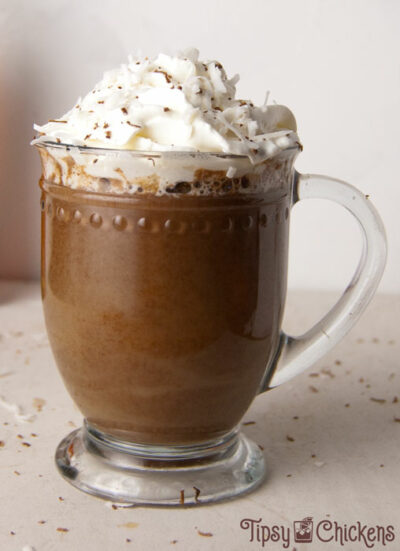 hot chocolate in a glass mug made with coconut milk, bakers chocolate, amaretto and coconut syrup topped with whipped cream and chocolate shavings