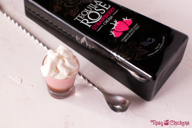 bottle of tequila rose with a chocolate strawberry shot topped with whipped cream with a bar spoon