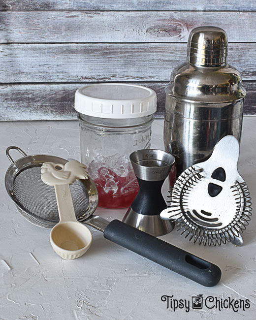 cocktail shaker, mason jar with screw on lid, jigger, hawthorn strainer, tablespoon and strainer set up to show how to make a home bar out of things you already have