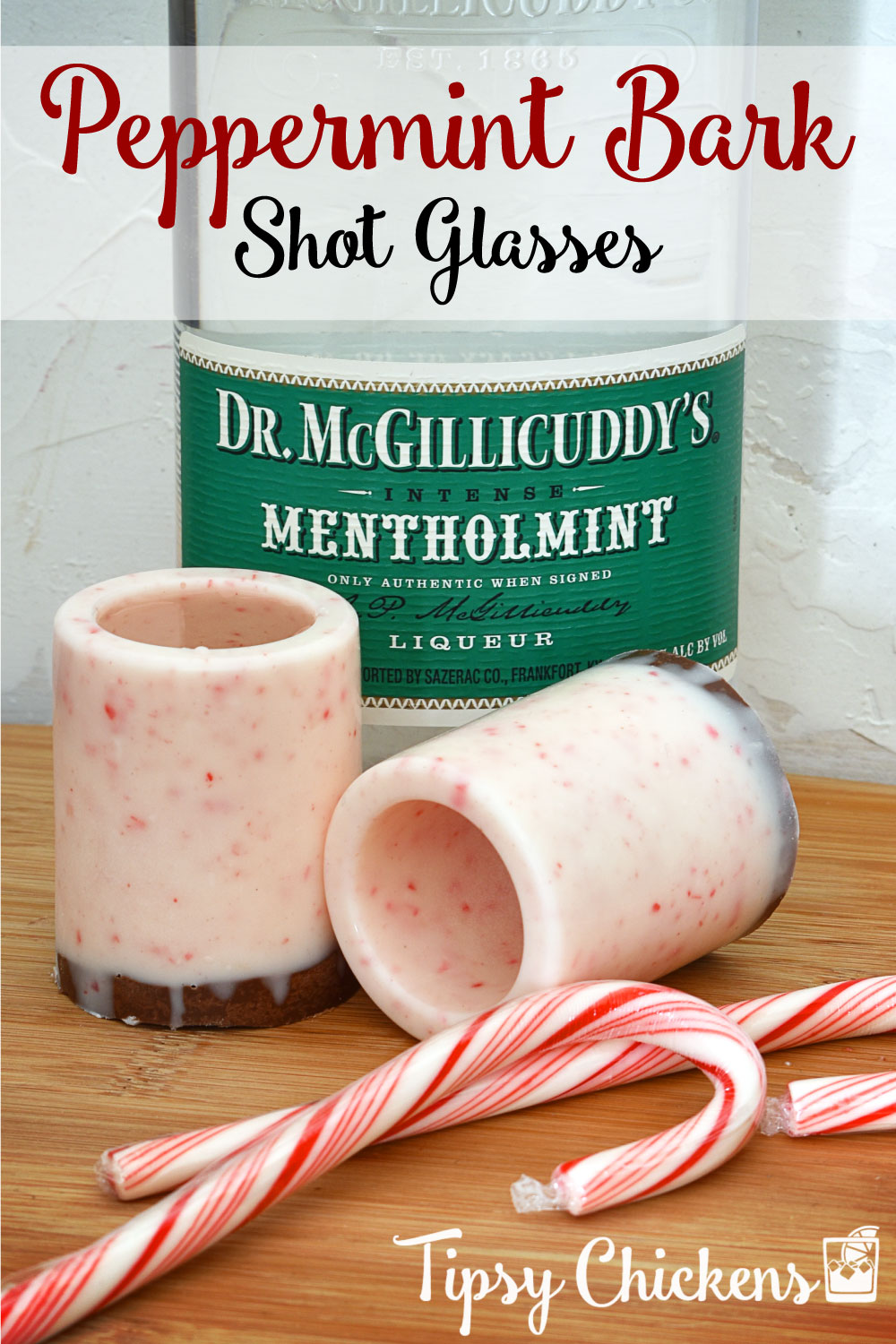 bottle of Dr. McGillicuddy's mentholmint behind two peppermint bark shot glasses made with almond bark and crushed candy canes on a cutting board with two candy canes